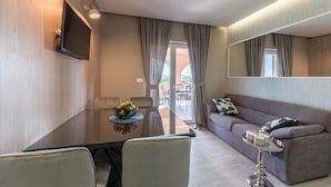Un salon moderne doté d’un téléviseur à écran plat fixé au mur, d’une table à manger avec des chaises et d’un canapé avec une petite table d’appoint.