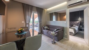 Une chambre d’hôtel moderne comprenant un coin repas, un canapé, un lit et une petite table sur laquelle se trouve un panier de fruits.