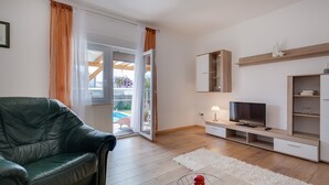 A modern living room with a leather sofa, a TV on a wooden stand, and a white rug. - Apartment Twisting By The Pool - Two bedroom apartment with private pool (Zadar)