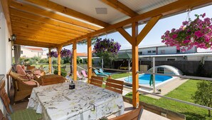 A covered outdoor seating area with a table and chairs, a pool, and hanging flowers. - Apartment Twisting By The Pool - Two bedroom apartment with private pool (Zadar)