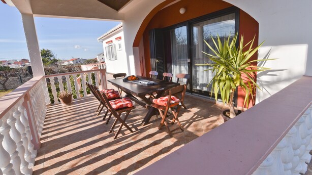 A covered outdoor dining area with a table and chairs, potted plants, and a view of the surrounding neighborhood. - Holiday Agava - Three Bedroom Apartment With terrace (Razanac)