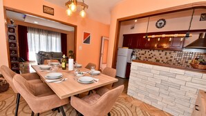 A dining area with a wooden table set for four, surrounded by cushioned chairs. A kitchen with a stone backsplash and wooden cabinets is visible in the background. - Holiday Agava - Three Bedroom Apartment With terrace (Razanac)