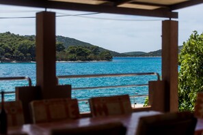 Ein Restaurant mit Außenbereich, das auf ein Gewässer und Hügel blickt.