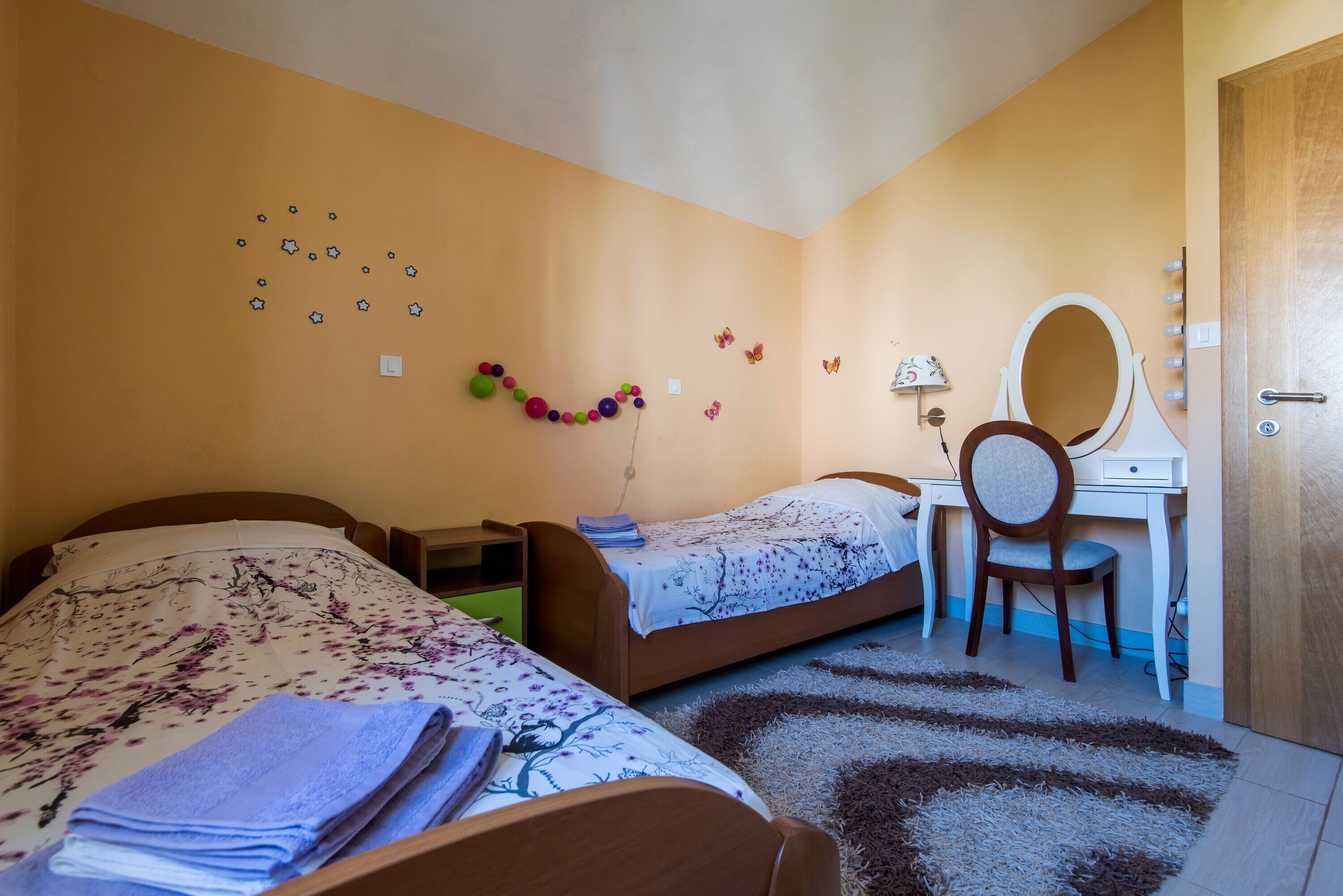 A bedroom with two beds, a desk with a mirror, and wall decorations including stars and butterflies.