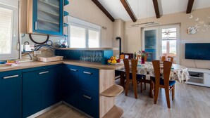 A modern kitchen with blue cabinets, a wooden dining table with chairs, and a TV in the dining area. - NOSTALGIJA three bedroom holiday home with sea view terrace (Brgulje)