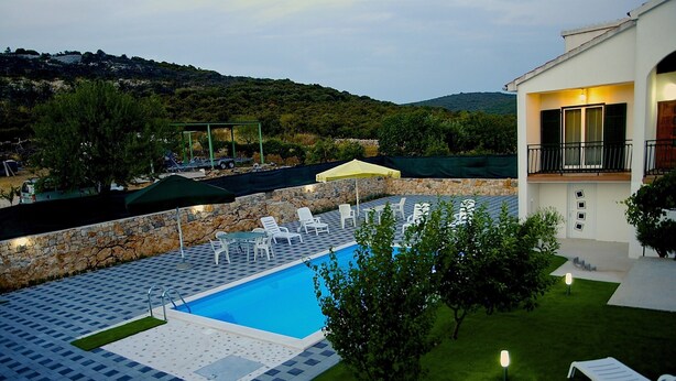 Zona de piscina con sillones de descanso, pared de piedra y vistas del paisaje circundante.