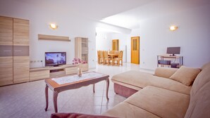 Una sala de estar moderna con un sofá, una mesa de centro de madera, un televisor y un comedor con sillas y una mesa.