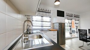 Una cocina moderna con un lavamanos de acero inoxidable, horno empotrado y refrigerador. Cuenta con un comedor con mesa y sillas.