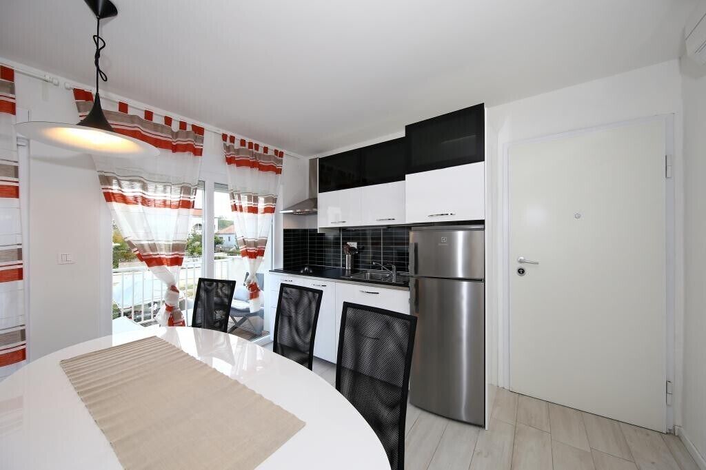 Een moderne keuken met witte kasten, een roestvrijstalen koelkast en een eethoek met een witte tafel en stoelen.
