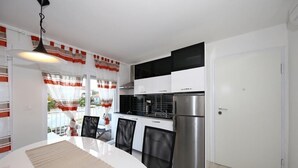 Een moderne keuken met witte kasten, een roestvrijstalen koelkast en een eethoek met een witte tafel en stoelen.