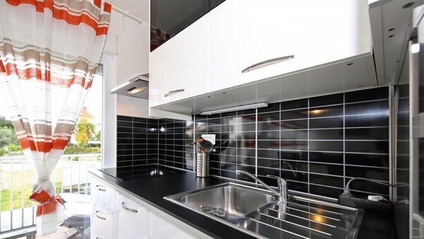 Een moderne keuken met een zwart betegelde spatwand, een roestvrijstalen spoelbak en witte kasten.