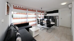Een moderne woonkamer met een zwarte bank, een witte salontafel en een eethoek met zwarte stoelen en een witte tafel.