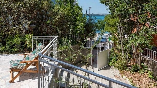Un balcon doté d’un sol en pierre, d’une rambarde en métal et offrant une vue sur un immeuble équipé de climatiseurs.