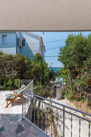 A balcony with a stone floor, a metal railing, and a view of a building with air conditioning units. - Villa Adriatica - Two Bedroom Villa  with Terrace and Balcony (Brodarica)