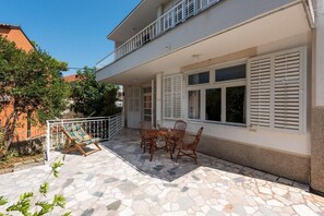 Un bâtiment à deux étages doté d’un balcon, d’une terrasse en pierre avec une table et des chaises, et d’une balustrade blanche.