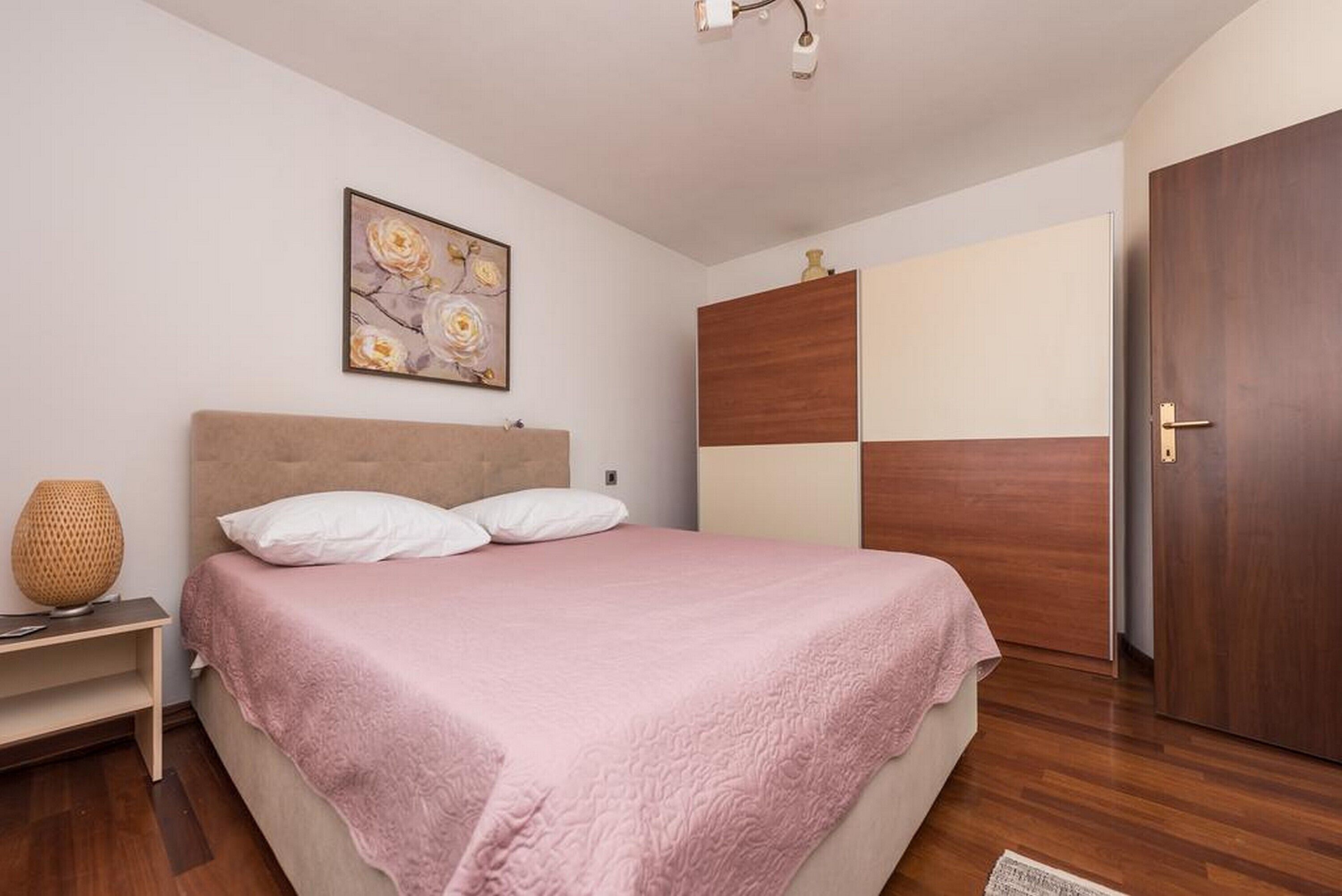 A bedroom with a bed, a bedside table, a lamp, a wardrobe, and a painting on the wall.