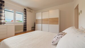 A bedroom with a large bed, a wardrobe, a radiator, and a window with curtains. - Apartment Villa Odesa - Two Bedroom Apartment with Balcony, shared Swimming Pool (Zadar)