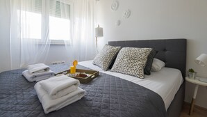 Ein ordentlich bezogenes Bett mit grauer Steudecke, weißen Kissen und einem Tablett mit einem Muffin und Orangensaft.