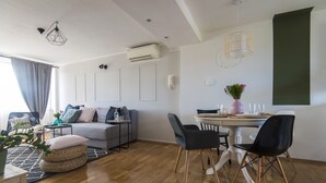 Ein modernes Wohnzimmer mit grauem Sofa, einem Esstisch mit Stühlen, einem Couchtisch und einer Topfpflanze.