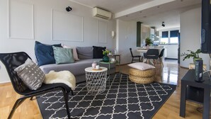 Ein modernes Wohnzimmer mit einer Couch, einem runden Couchtisch, einem schwarz-weißen Teppich und einem schwarzen Sessel.