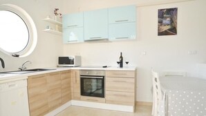 Een compacte keuken met een ingebouwde oven, een magnetron en een spoelbak. Er is een eethoek met een tafel en stoelen.