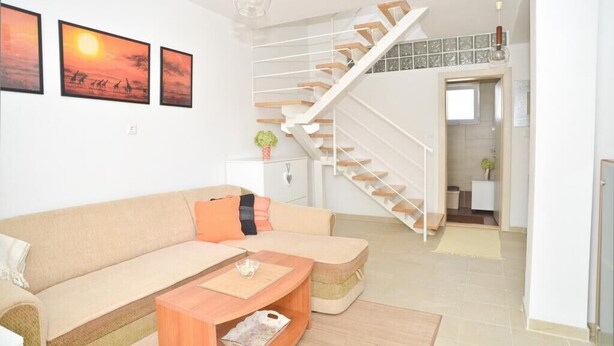 Een moderne woonkamer met een bank, salontafel en een trap naar een verdieping erboven.