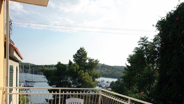 Ein Balkon mit Tisch und Stühlen, der auf einen Yachthafen mit Booten und Bäumen blickt.