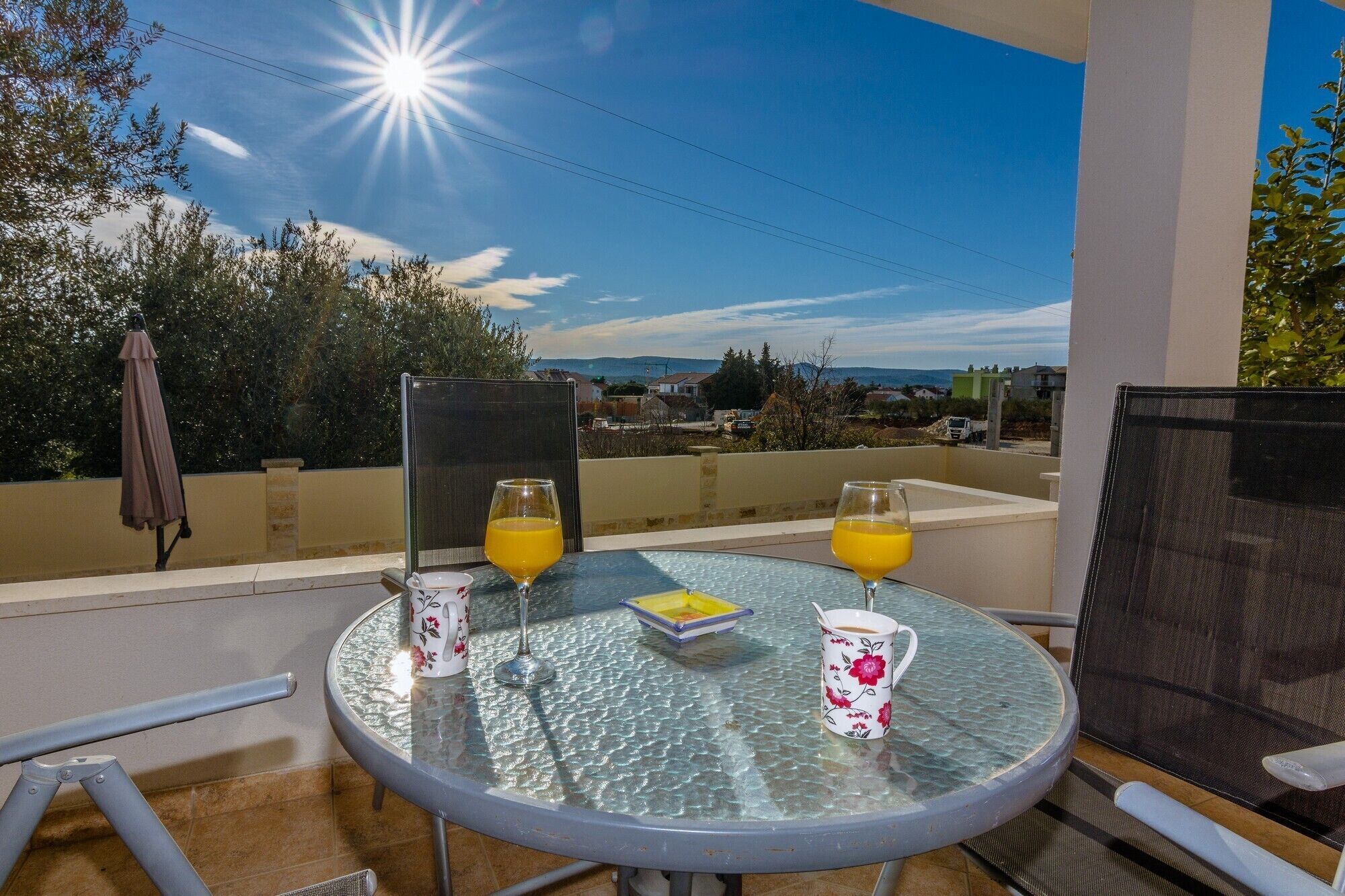 A balcony with a glass table, two chairs, and two glasses of orange juice.