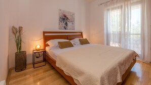 Une chambre à coucher avec un lit en bois, une table de chevet avec une lampe, un climatiseur fixé au mur et une fenêtre avec des rideaux légers.