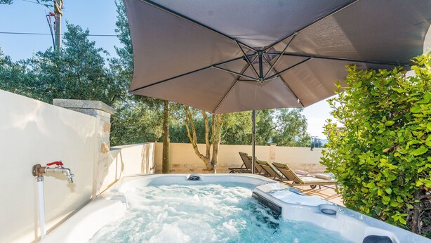 Un bain à remous équipé d’une pompe, entouré d’une terrasse avec des chaises longues et un parasol.