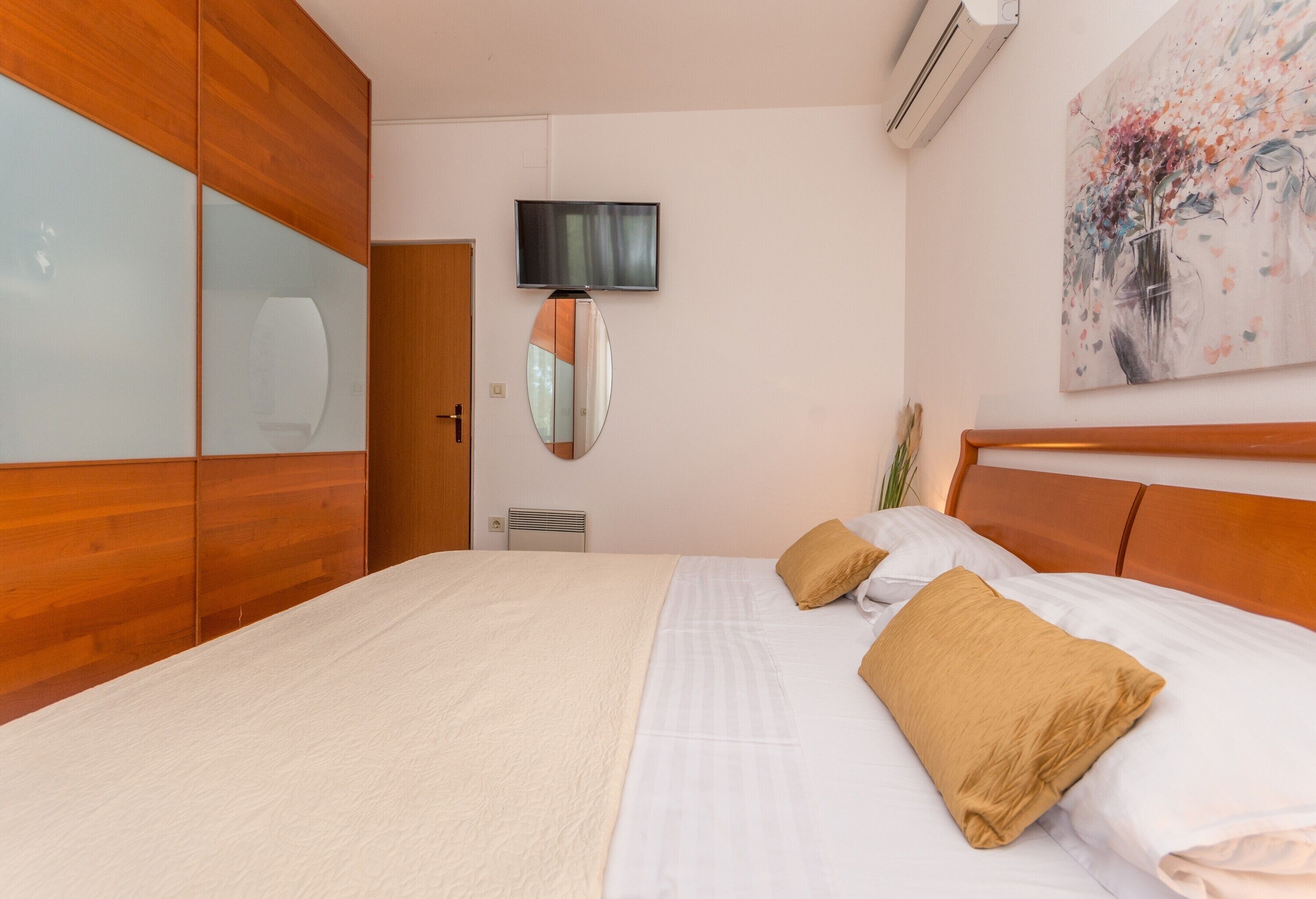 A hotel room with a bed, wooden wardrobe, a television, a mirror, and a painting on the wall.