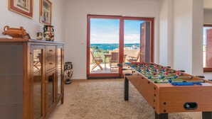 Une pièce équipée d’un baby-foot, d’une armoire et donnant, par une porte vitrée, sur un espace extérieur aménagé en coin salon.