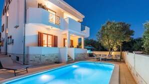 Une maison à deux étages avec une piscine, un espace salon extérieur et un balcon bien éclairé.