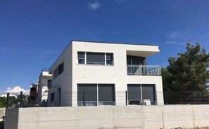 Ein modernes, zweistöckiges Gebäude mit einem Balkon im oberen Bereich, großen Garagentoren und blauem Himmel im Hintergrund.