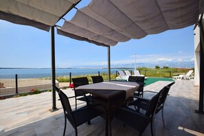 Eine Terrassensitzgelegenheit im Freien mit Tisch und Stühlen, mit Blick auf ein Gewässer und eine entfernte Landschaft.