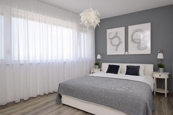 Ein modernes Schlafzimmer mit einem großen Bett, weißen Vorhängen, zwei Wandbildern und Nachttischlampen.