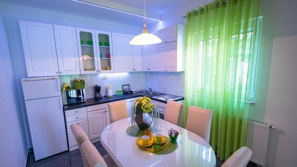 Una cocina moderna con armarios blancos, una mesa de comedor con sillas y una cortina verde.