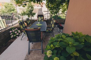 An outdoor patio with a table and chairs, a grill, and potted plants.
