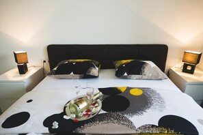 Ein ordentlich bezogenes Bett mit einer schwarz-weißen Bettdecke, zwei Nachttischlampen und einem Tablett mit einer Flasche und Gläsern auf dem Bett.