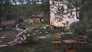 A garden with a wooden table and two chairs, surrounded by greenery and rocks.