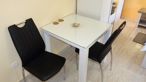 Un pequeño comedor con una mesa blanca y dos sillas negras. Hay un cuenco pequeño con galletas sobre la mesa.