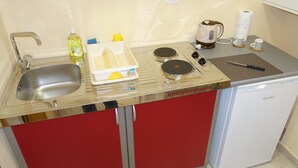Una kitchenette compacta con un lavamanos, una cafetera, un hervidor y un refrigerador pequeño.