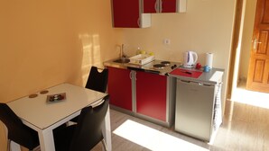 Une cuisine de taille réduite avec une table et des chaises blanches, un petit réfrigérateur et des placards rouges.