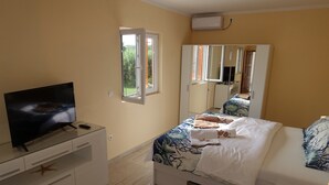 Une chambre à coucher avec un lit, un téléviseur posé sur une commode blanche, une fenêtre et un miroir.