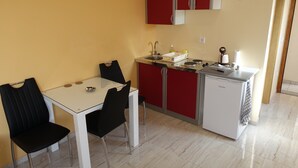 Una cocina compacta con una mesa blanca y sillas negras, armarios rojos y un refrigerador pequeño.