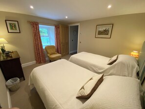 A hotel room with two beds, a chair, a lamp, and a window with curtains. - Littleton Cottage (Ballater)