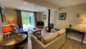 Una sala de estar acogedora con sofá, mesa de centro, televisor, chimenea y vistas al exterior.