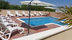 A rooftop pool area with white lounge chairs and umbrellas, surrounded by a tiled deck.