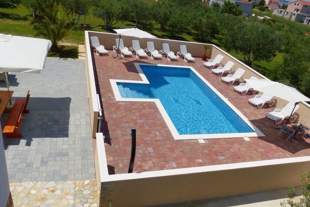Una piscina en la azotea con diseño geométrico, rodeada de sillones blancos y un solárium con baldosas.