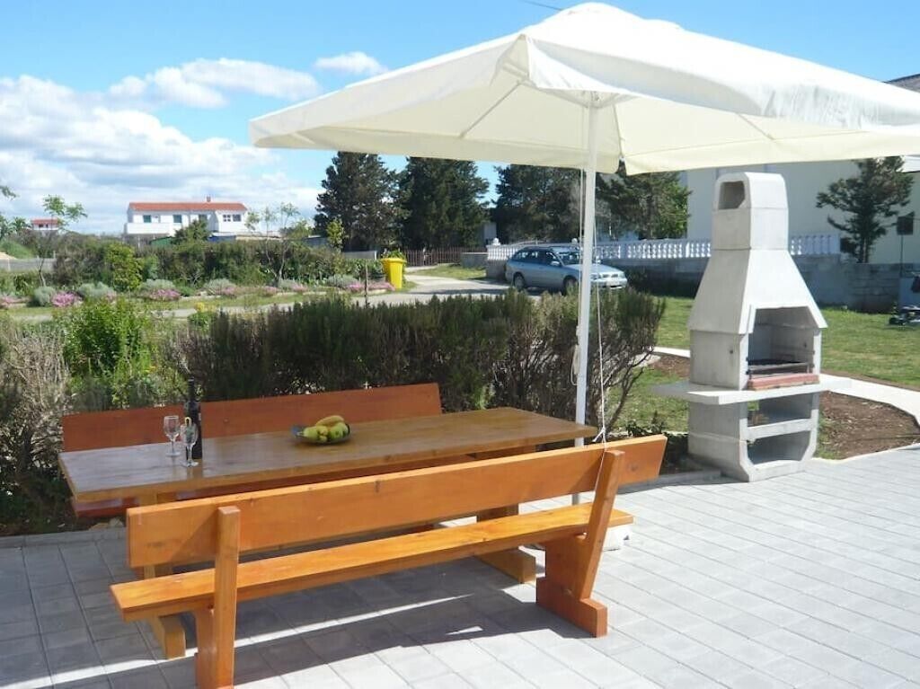 Une terrasse extérieure avec une table et des bancs en bois, un parasol blanc et un barbecue.